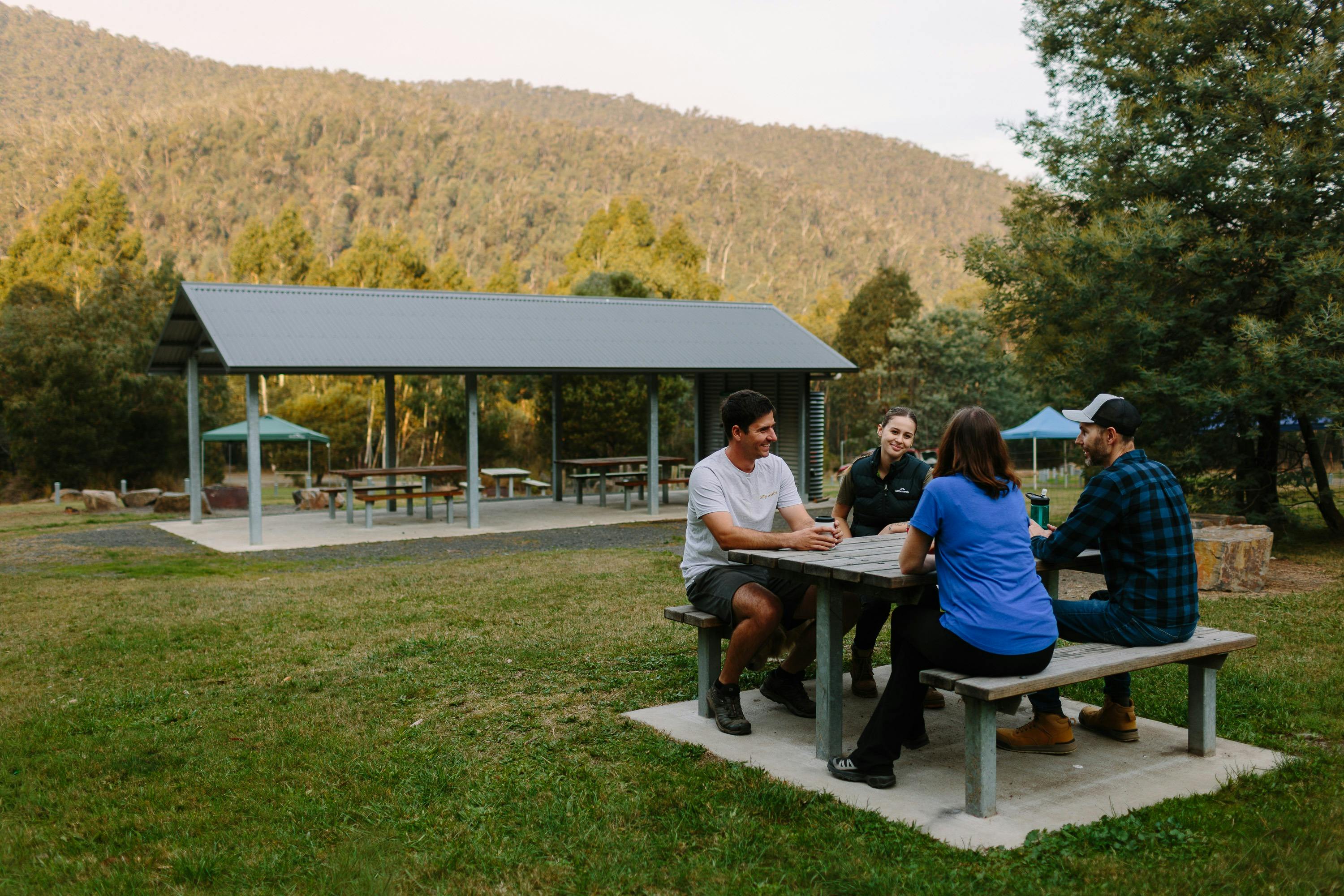 Group of people sitting at a picnic table with a large shelter in the background