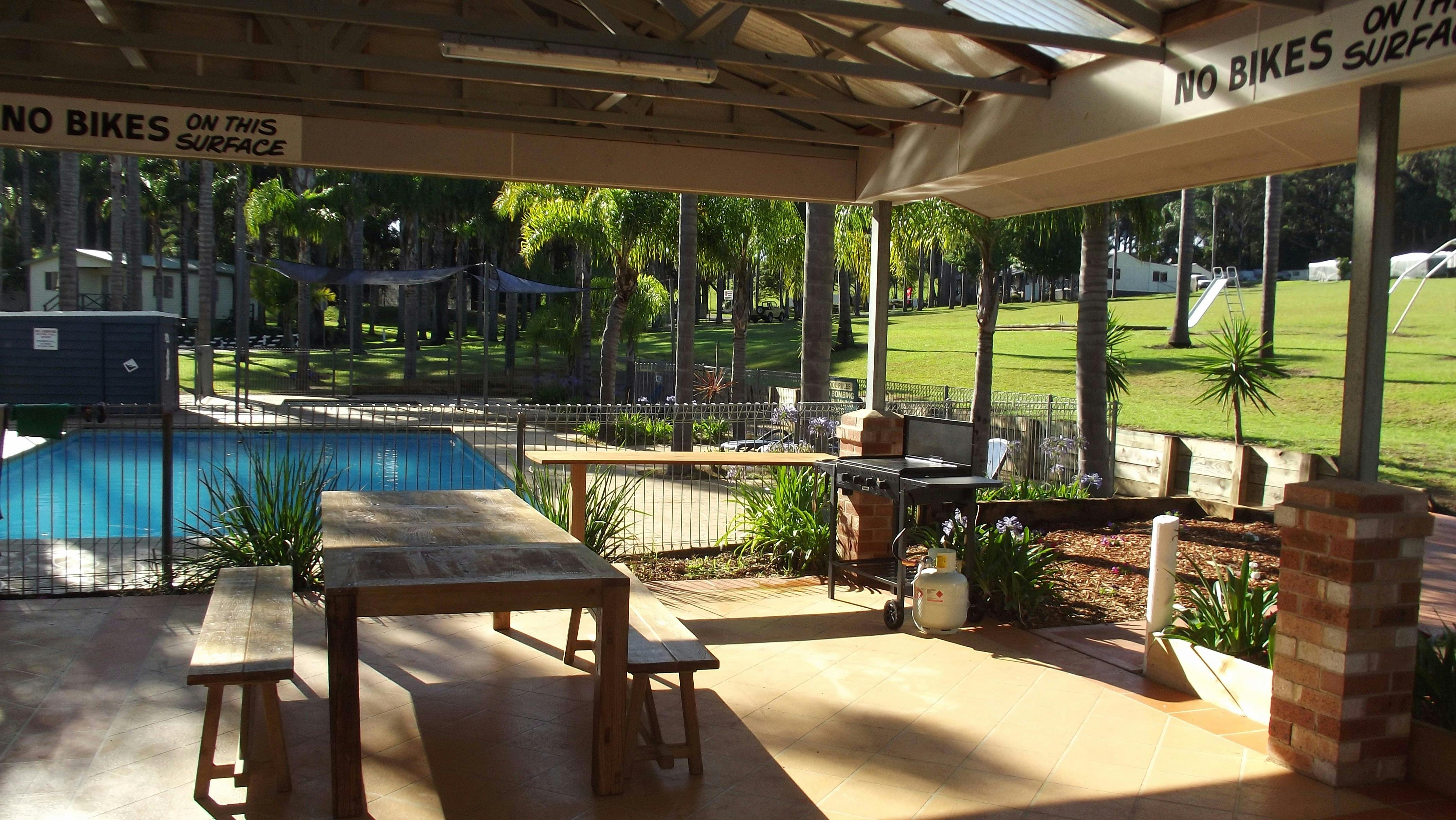 Covered outdoor BBQ and seating area next to camp kitchen and pool