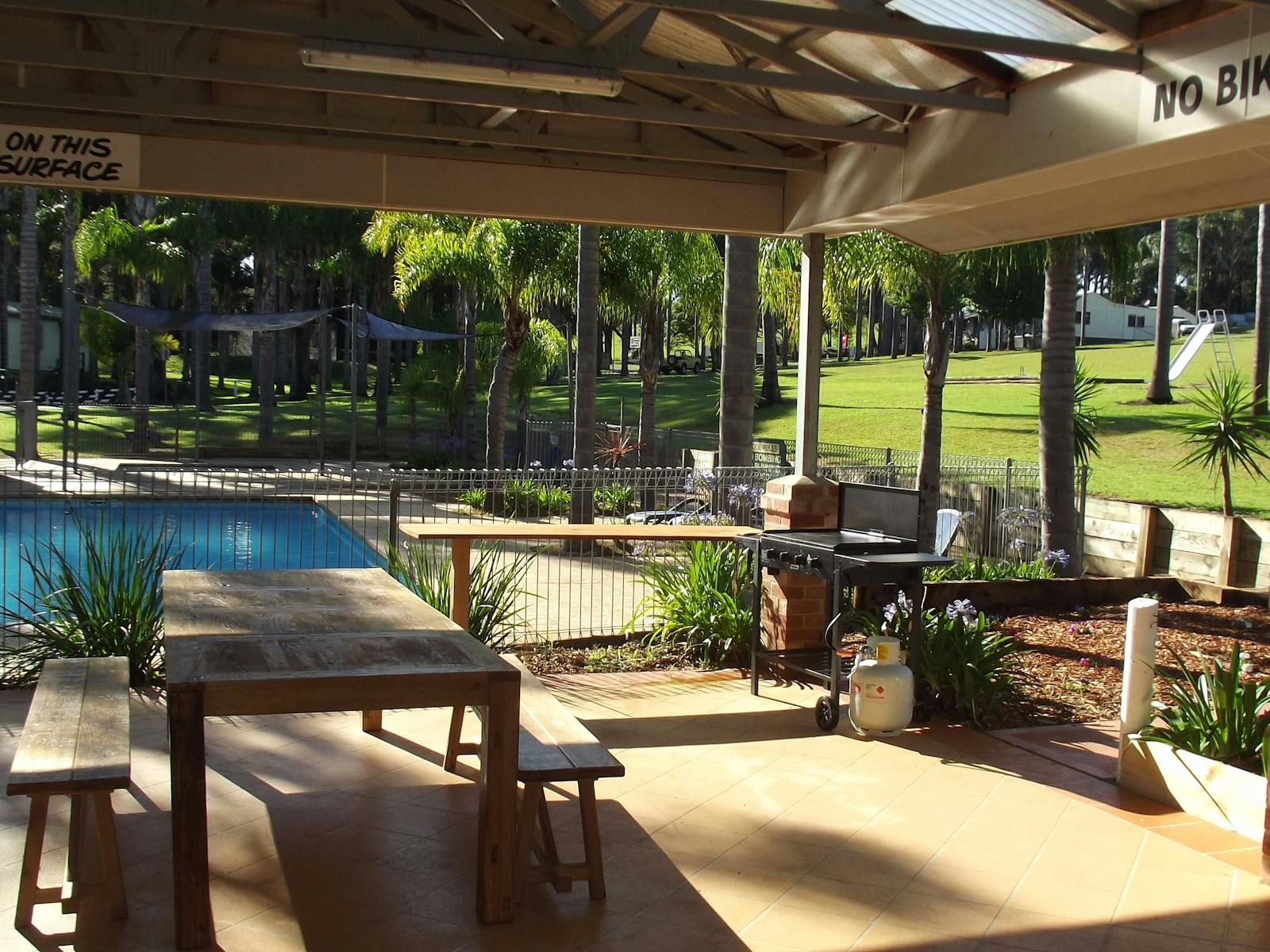 Covered outdoor BBQ and seating area next to camp kitchen and pool