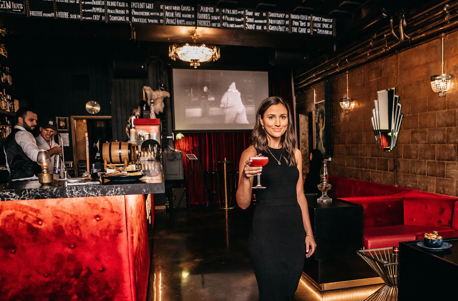 Smiling Waitress delivering a cocktail to a customer. Black & white movie playing, chandelier.