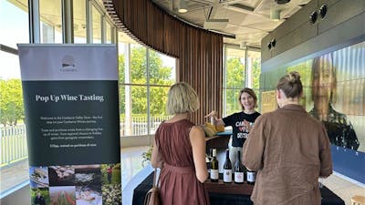 Two people chatting to a vitner over bottles of wine.