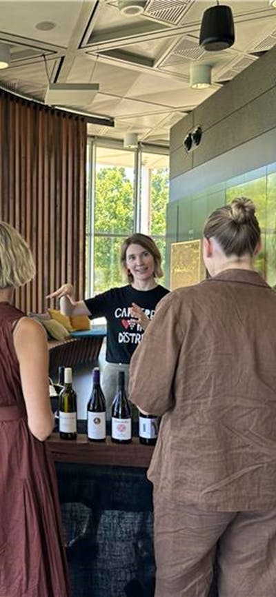Two people chatting to a vitner over bottles of wine.