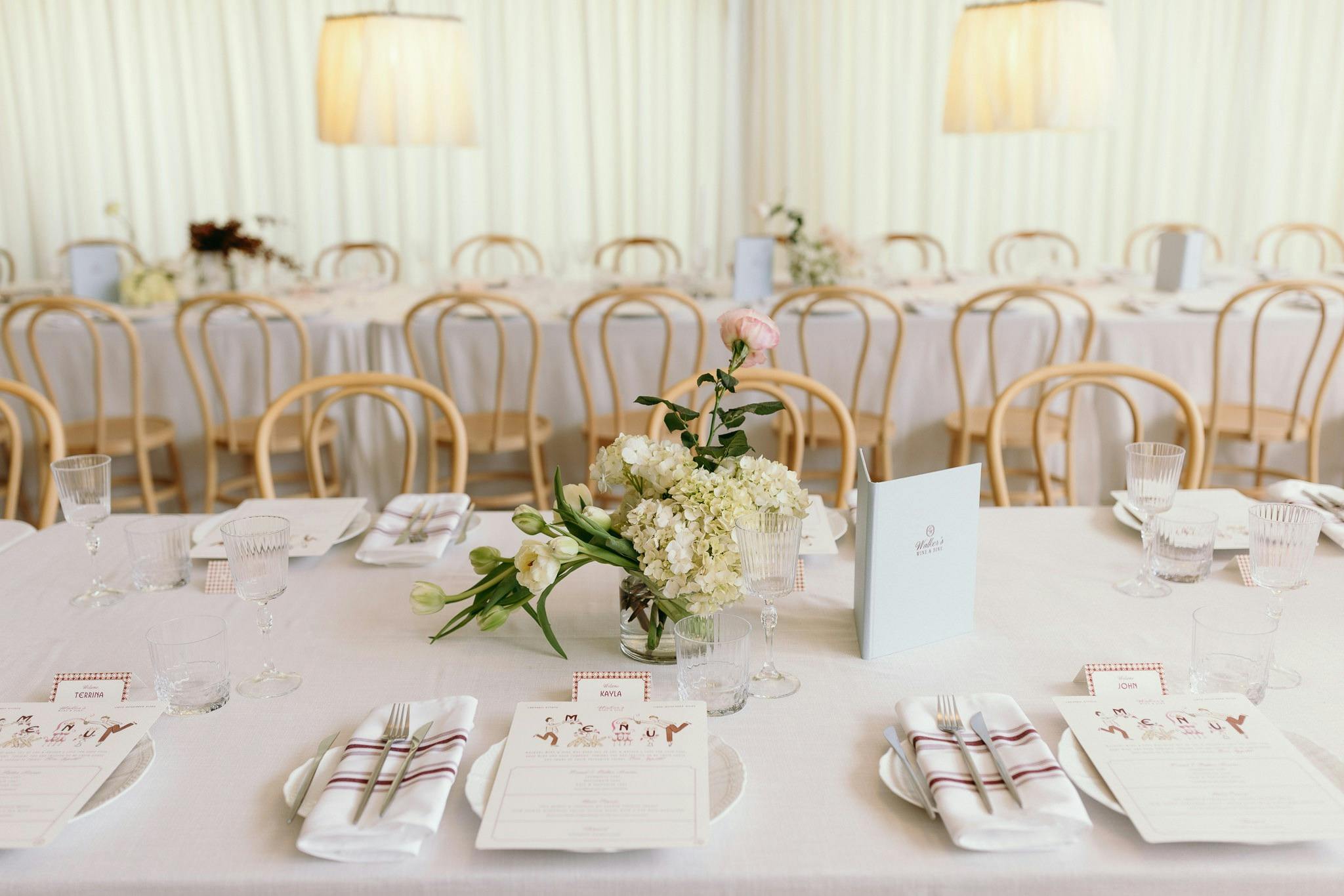 Wedding event setup with long white tables and timber beechwood chairs with floral dressings
