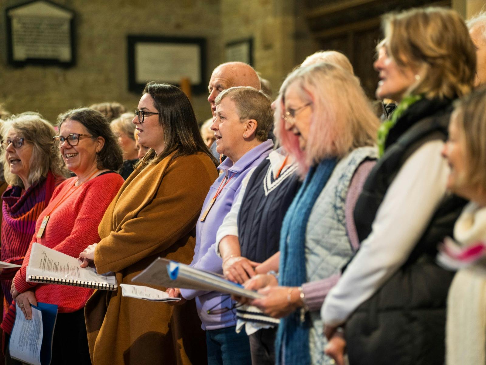 Close-up of adult choir members singing enthusiastically in a church or stone hall.