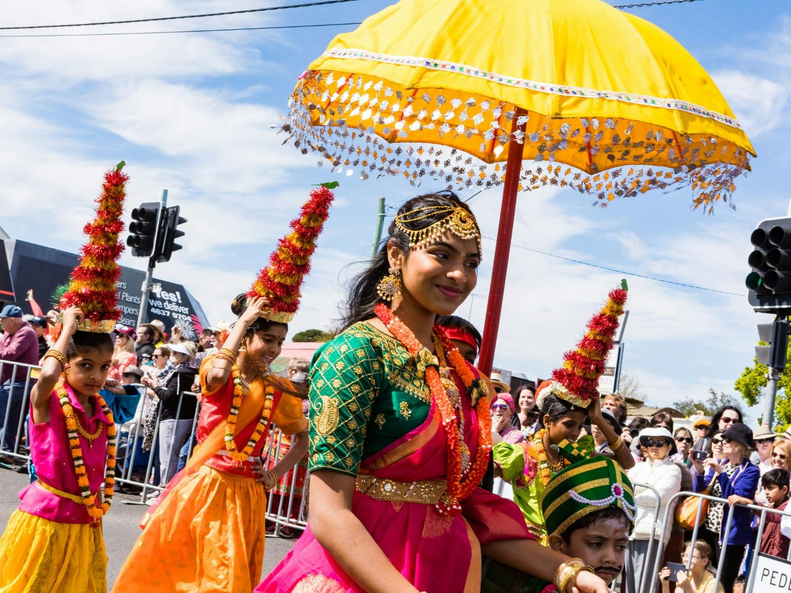 A women and several children in bright cultural dress take part in a floral street parade.
