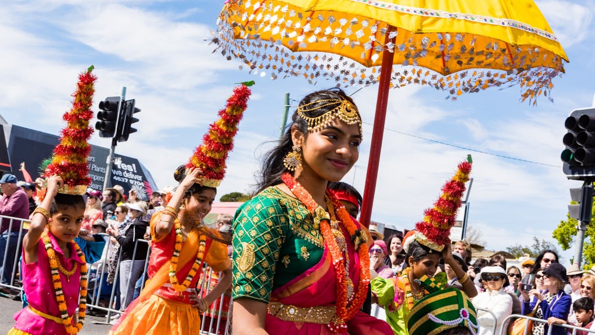 A women and several children in bright cultural dress take part in a floral street parade.
