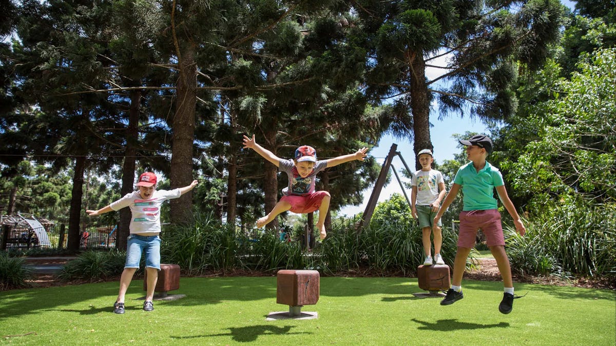 Four kids jumping into the air off timber blocks onto grass