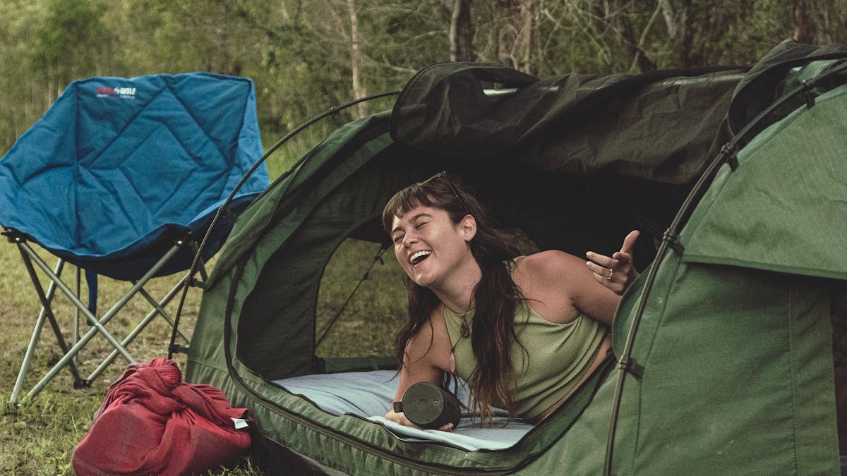 A happy girl in a swag with the bed made and a chair, relaxing enjoying her set up camp
