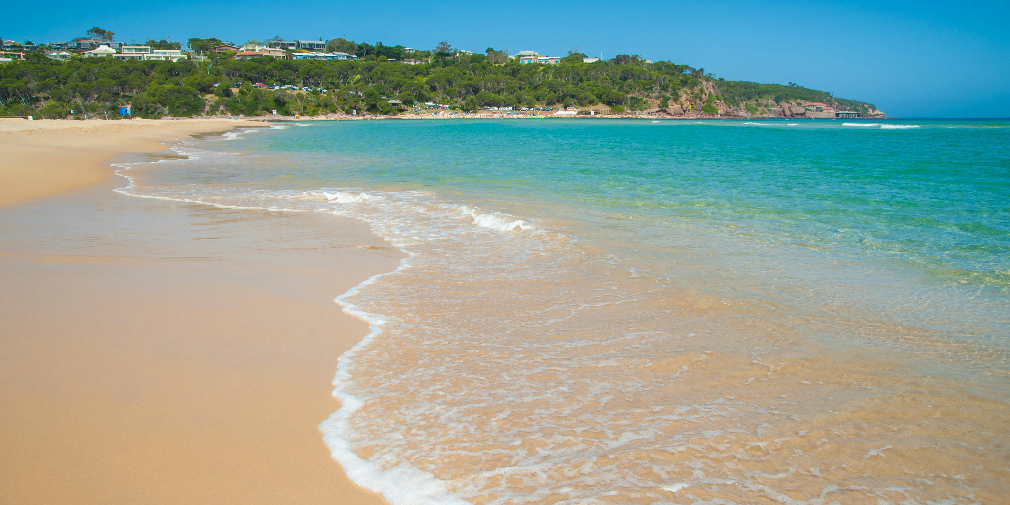 Beach at Merimbula on the Sapphire Coast showing the aqua-coloured ocean and the blue sky.