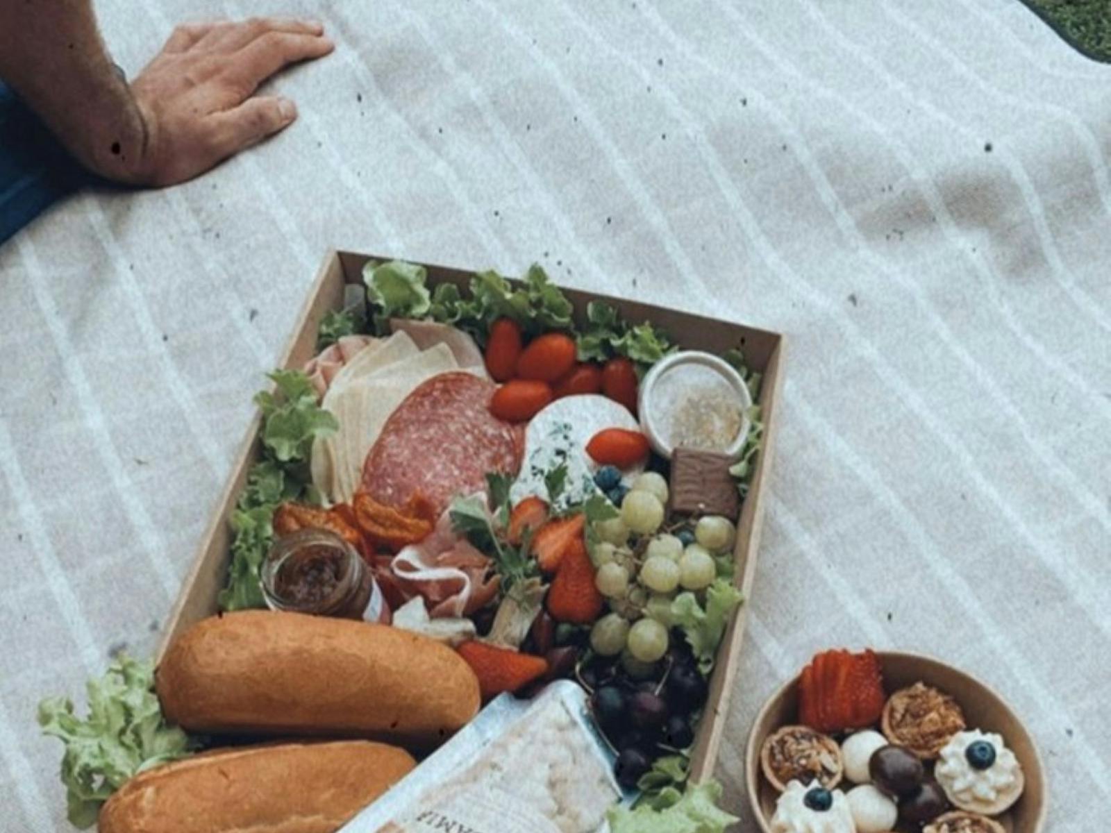 Close up of a picnic box filled with farm fresh produce laid out on a grey striped picnic rug