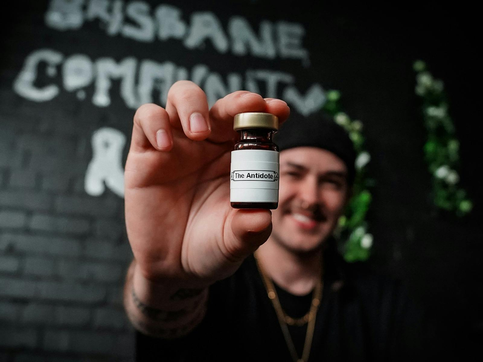 A person in a backwards black cap holding a pill bottle towards the camera, labelled the antidote
