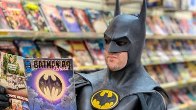 A man dressed as Batman reads a comic book inside a comic shop