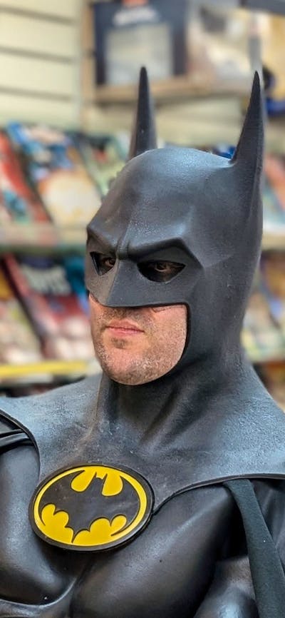 A man dressed as Batman reads a comic book inside a comic shop