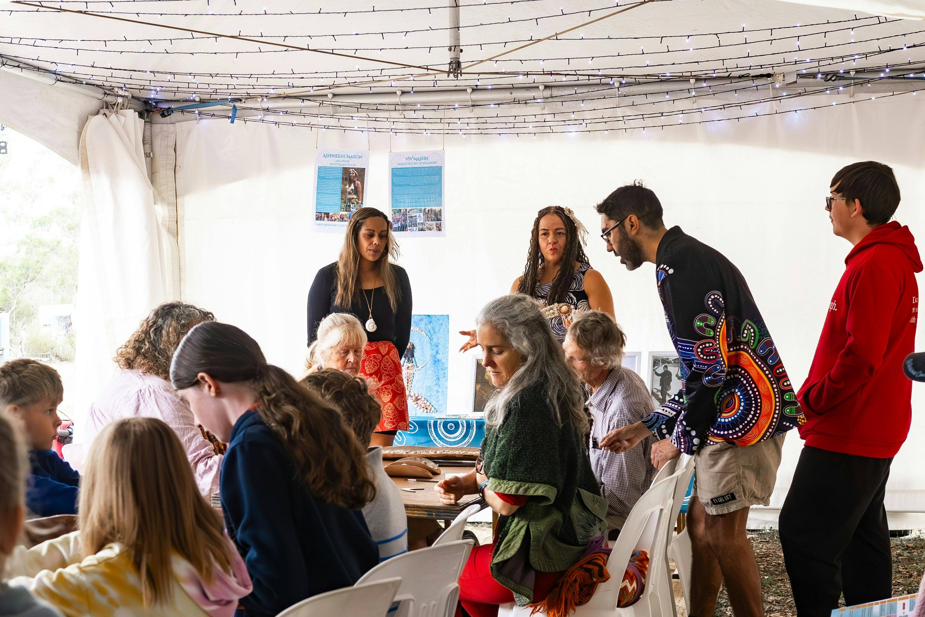 Two Aboriginal women conducting a shell working workshop in a marquee.