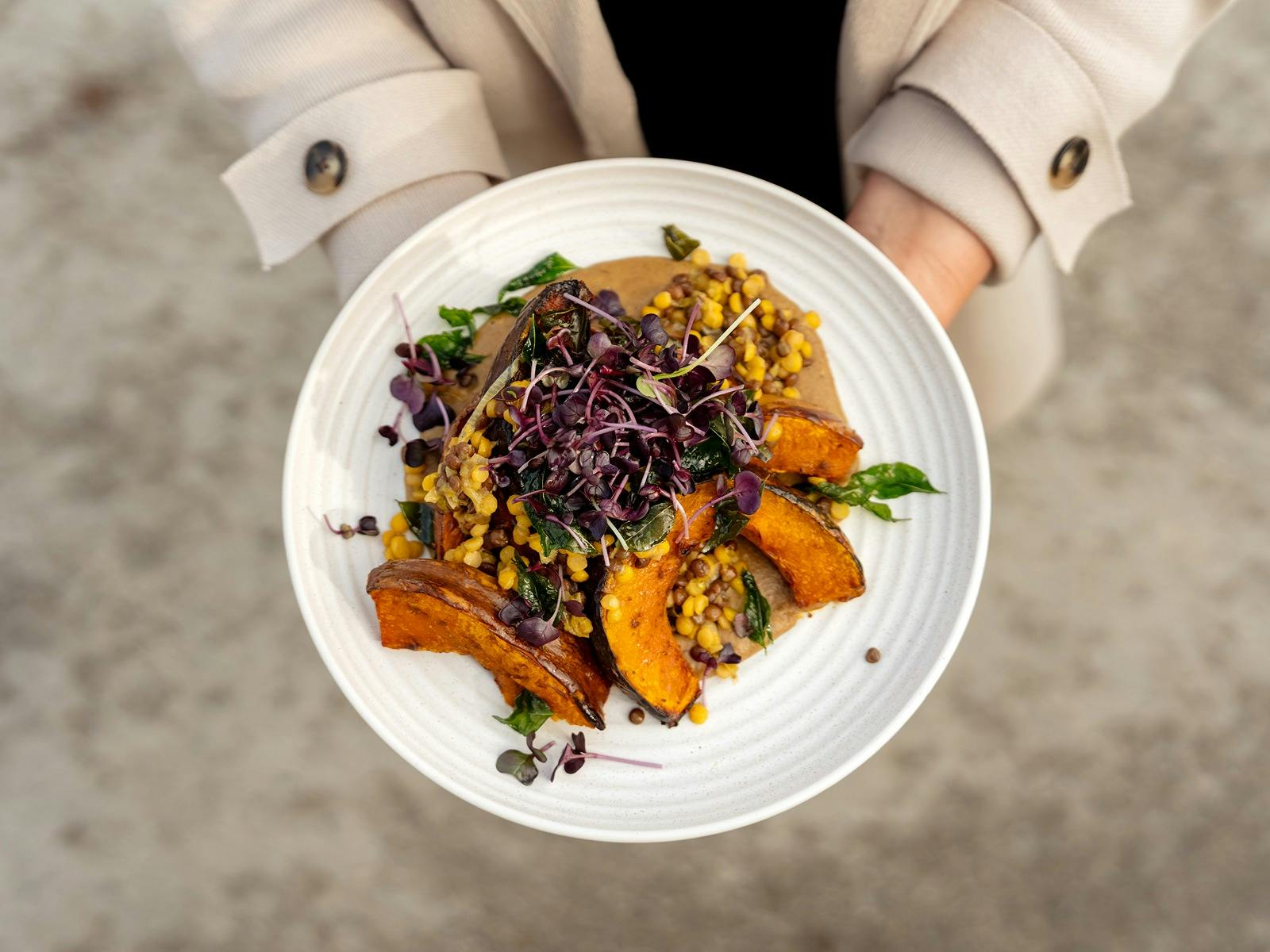 Roasted pumpkin with grains, corn and microgreens in a white bowl