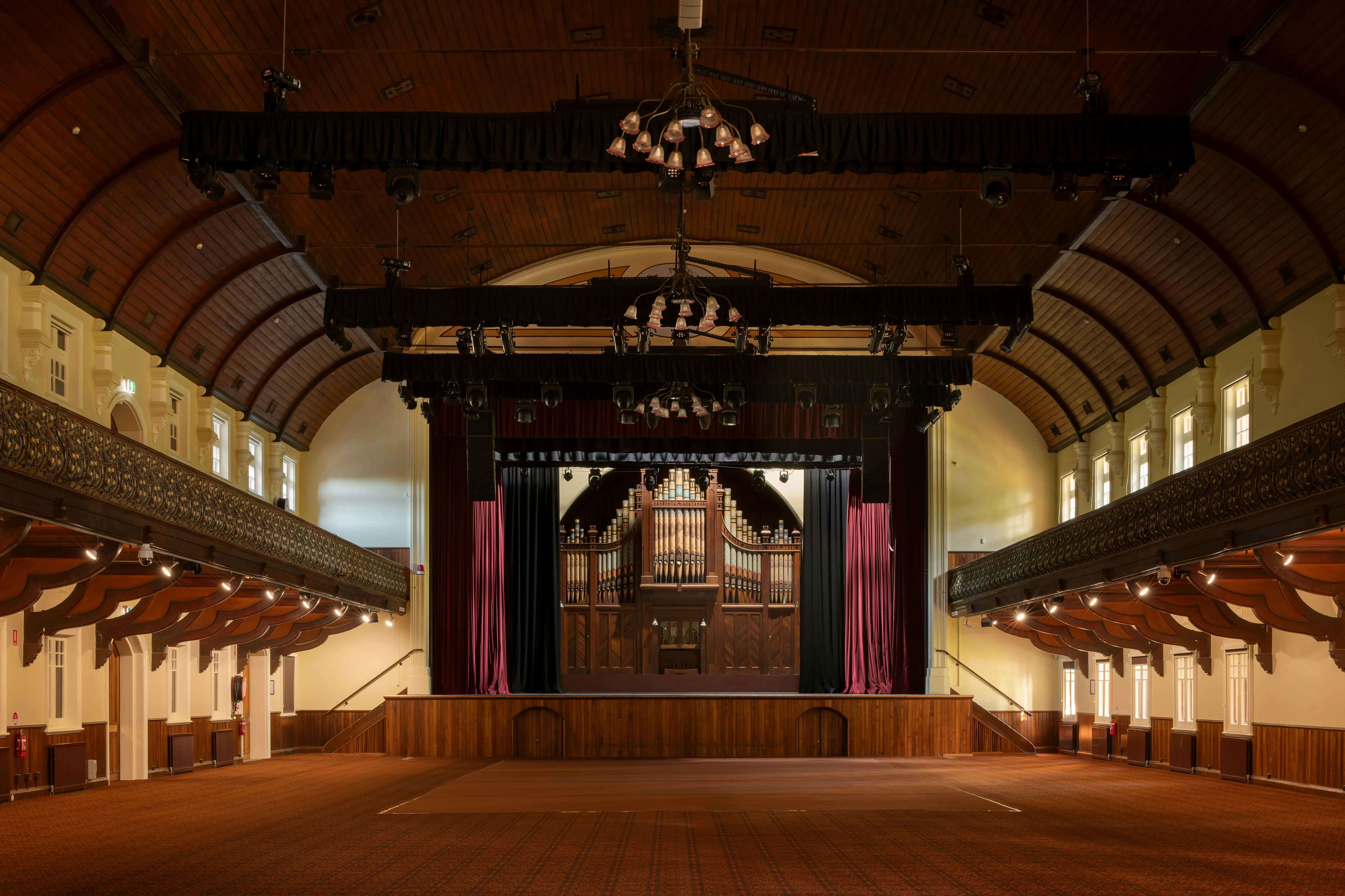 A grand community hall with high, wood ceilings and a stage at on end.