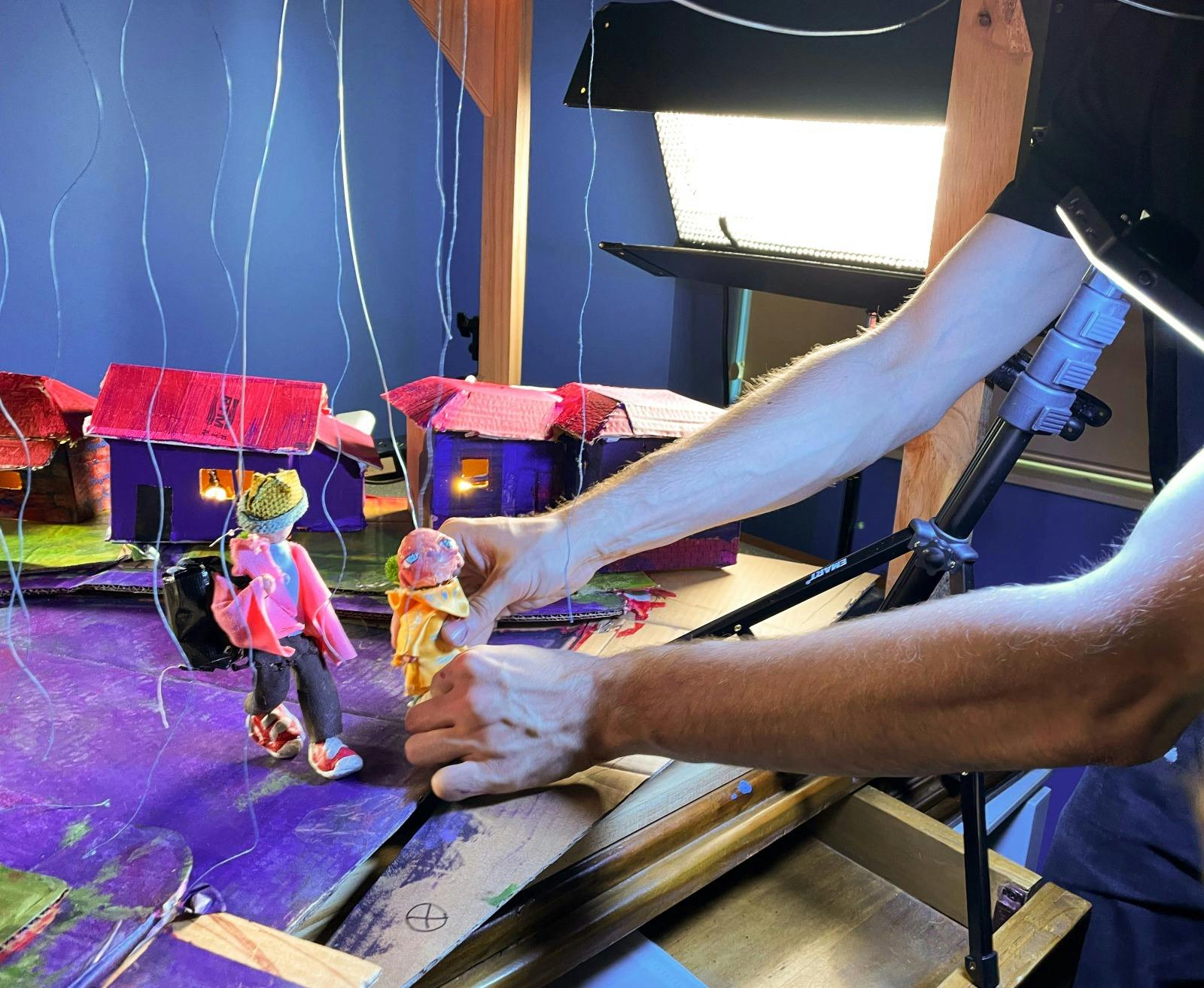 Filmmaker positioning two armature puppets on a set