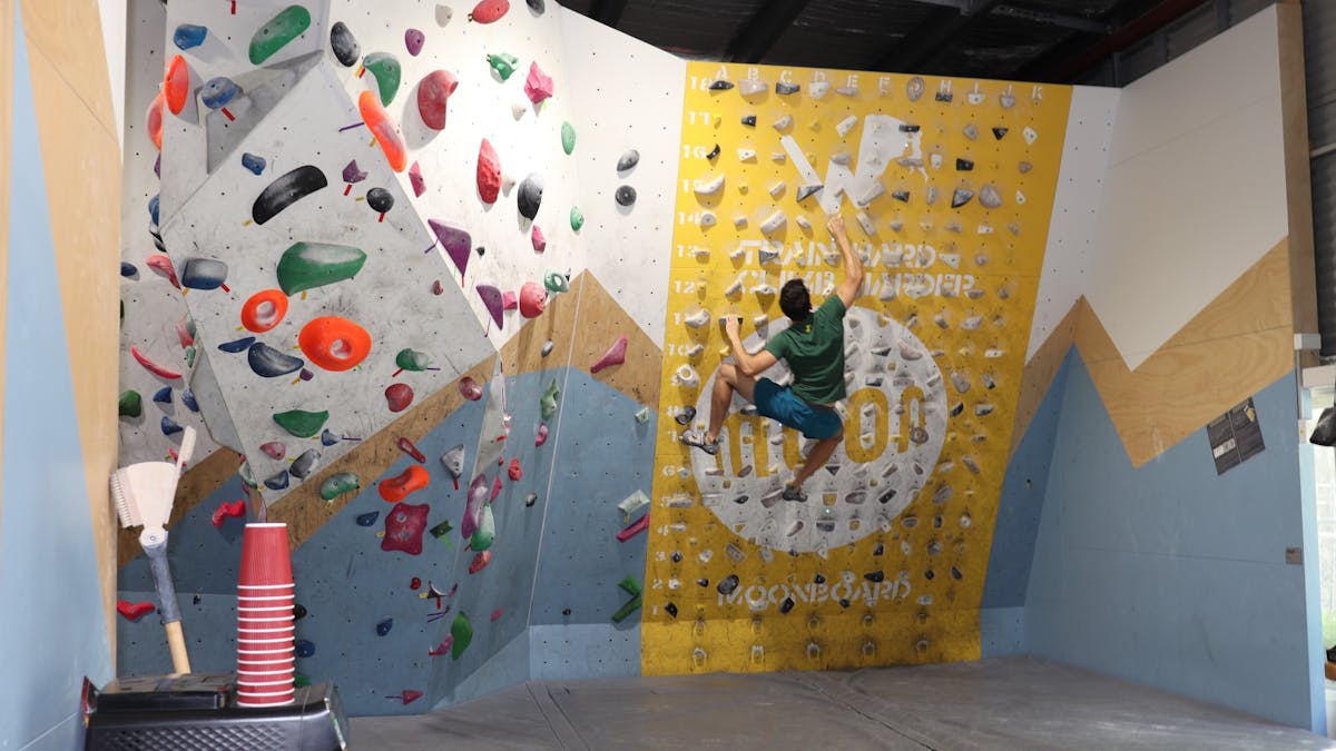 A climber using the 25 degree MoonBoard and is halfway up a difficult route.