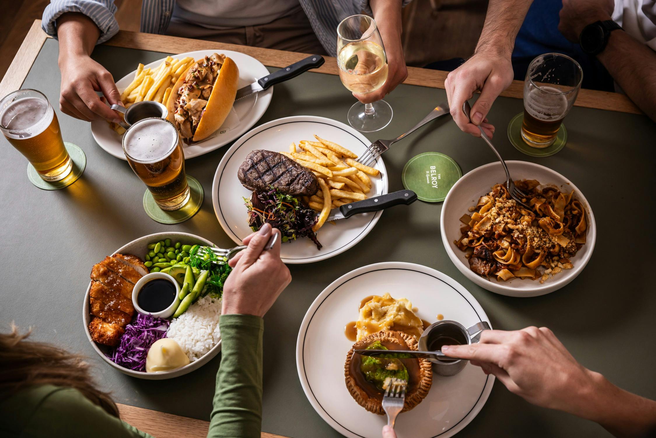 Plates of steak frites, pasta, pie, rotisserie chicken roll and poke bowl with beers and wines.