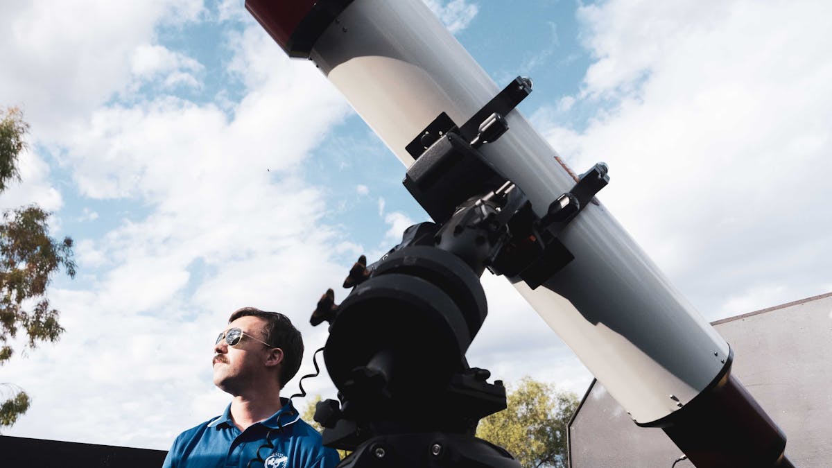 Guide standing beside one of the largest H-alpha telescopes in the world, looking up to the sky.