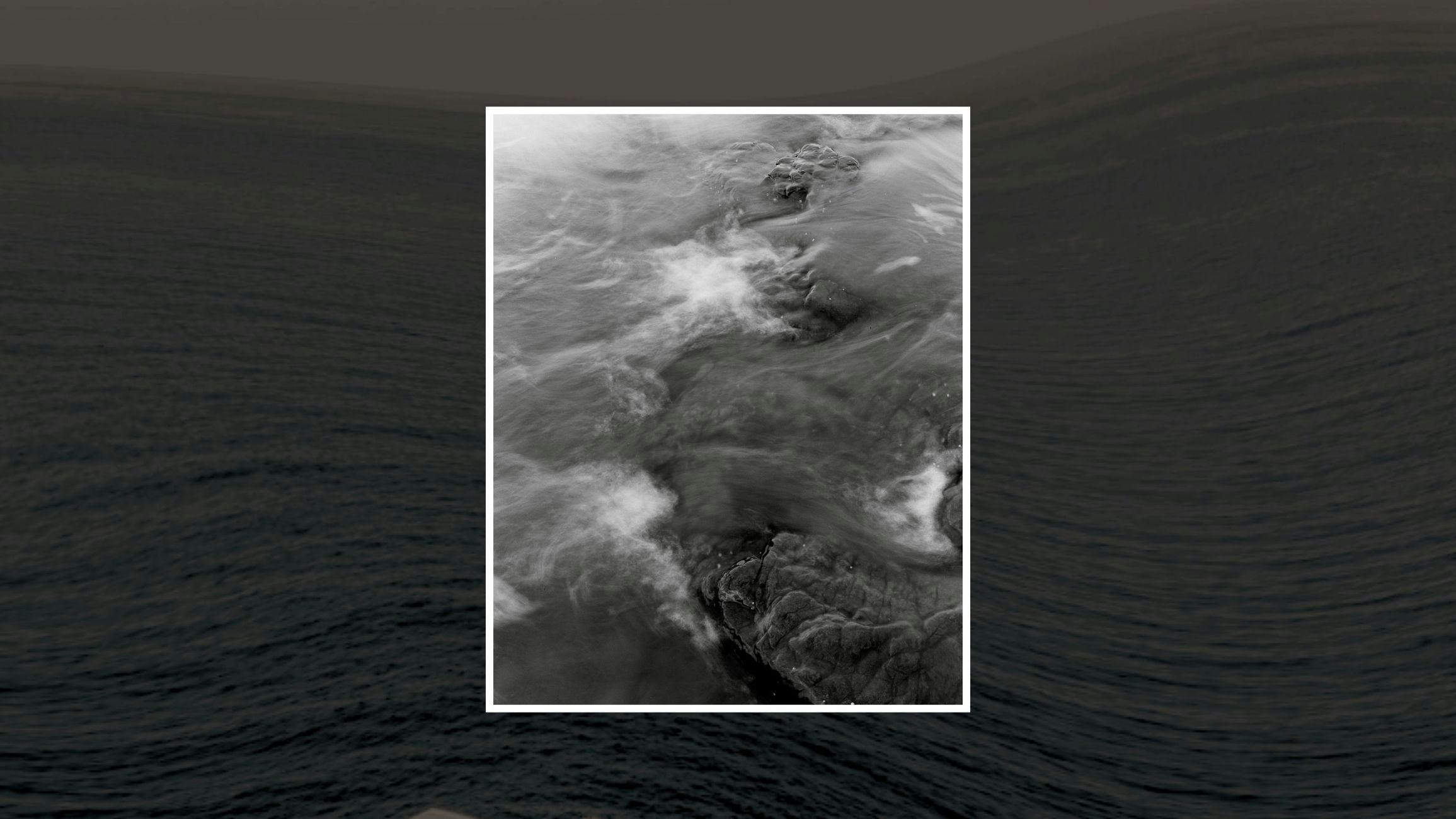 Black and white photo of ocean waves over rocks, with motion blur and a dark sea background.