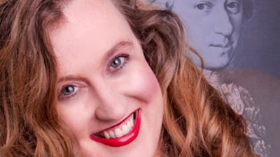 A portrait of a smiling woman with wavy brown hair and bright red lipstick.