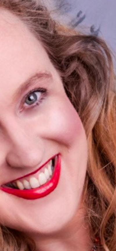 A portrait of a smiling woman with wavy brown hair and bright red lipstick.