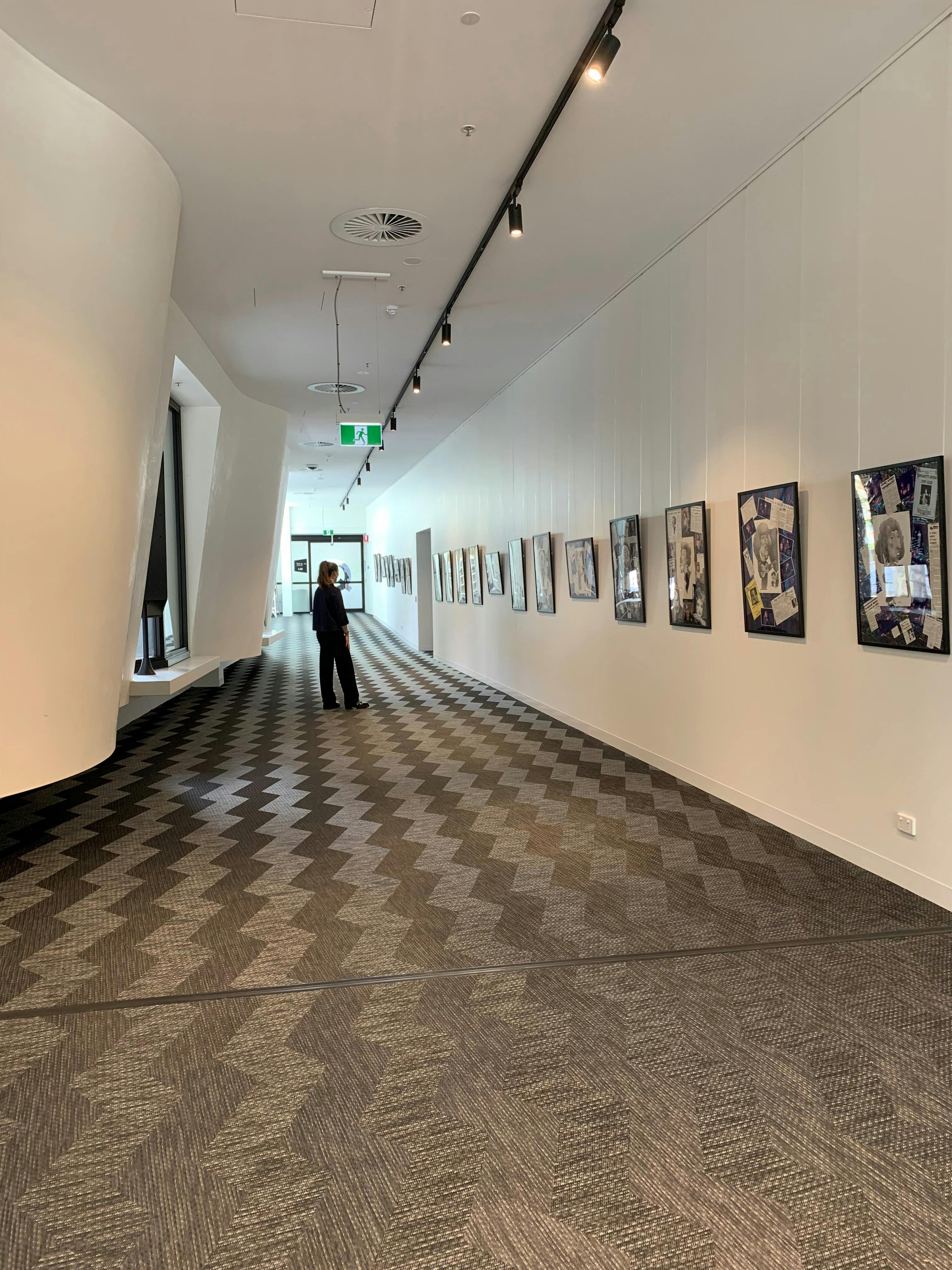 Interior gallery photo looking west with person in mid ground on patterned grey floor
