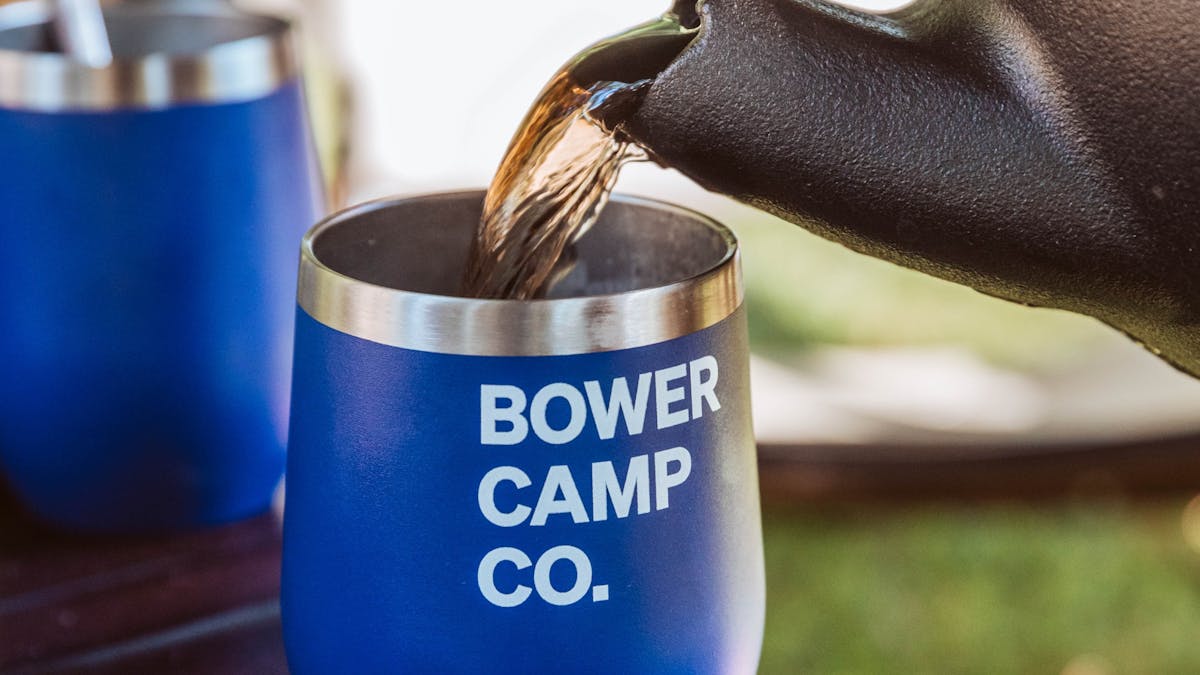 Tea pouring into a blue cup with Bower Camp Co. written on it