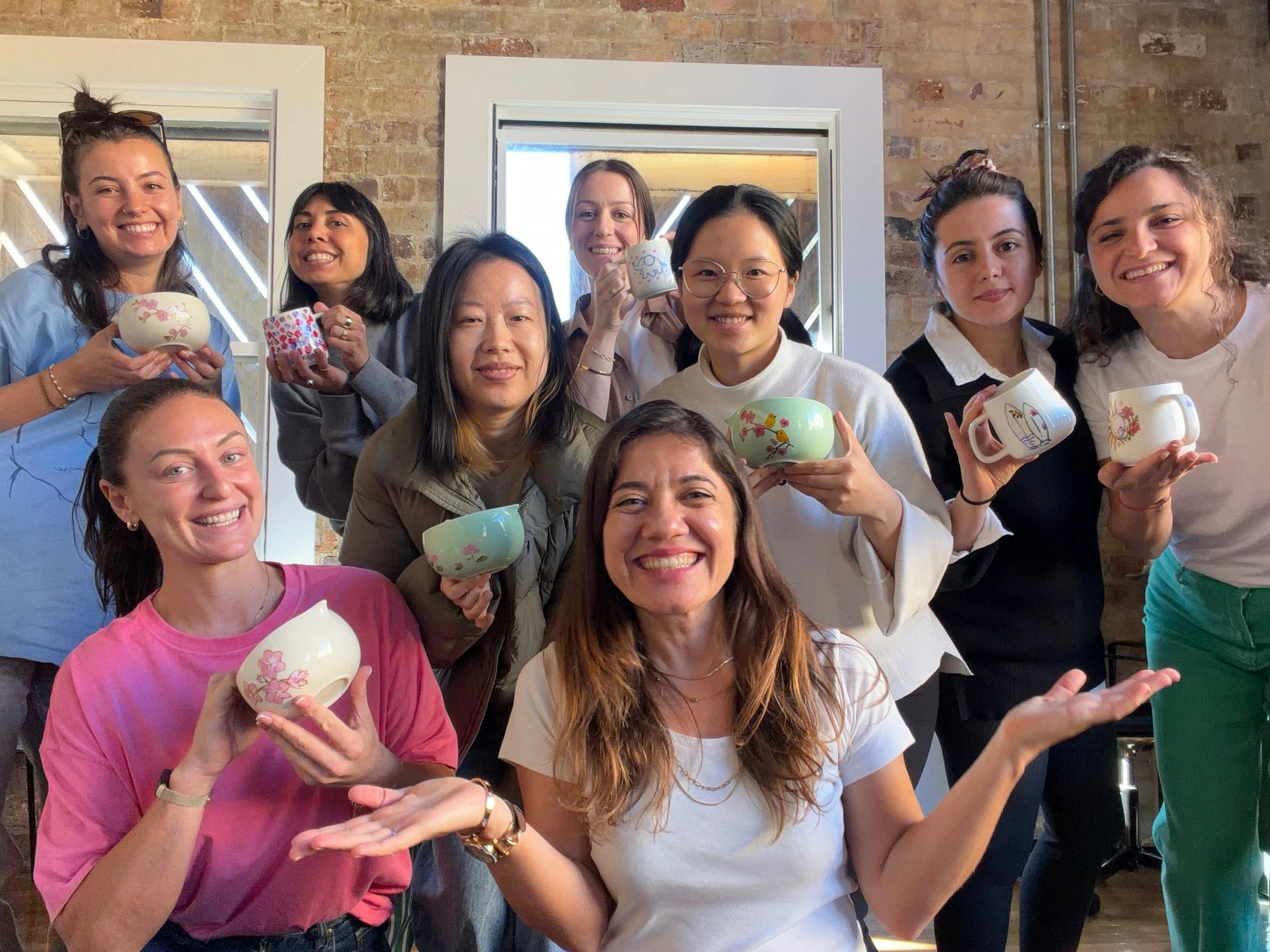 A smiling group of women holding hand-painted ceramic mugs and matcha bowls