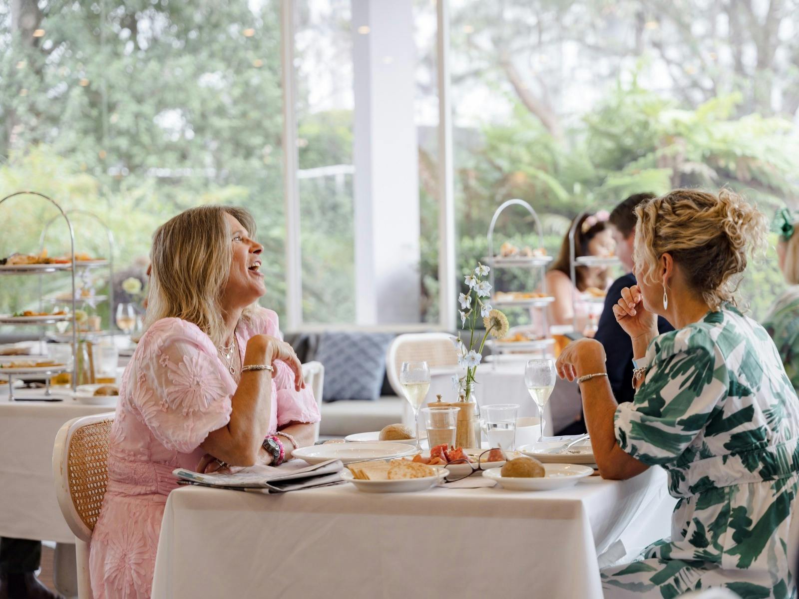 Two women enjoying lunch and conversation at a restaurant table, with glasses of wine, plated food a