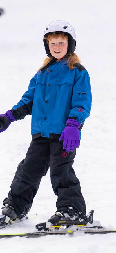 A boy skis on a gentle slope in a snowplough stance. The background is covered in snow.