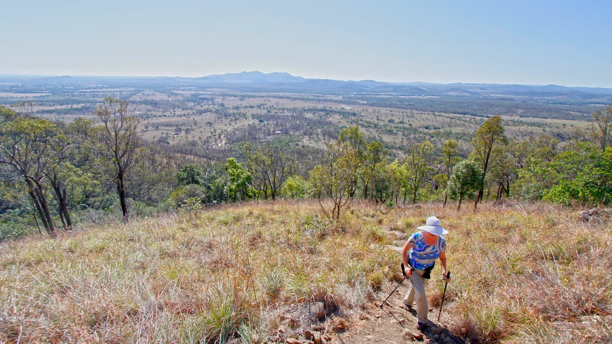 Walker on a track strides up a mountain slope with mountains and valleys in the distance.