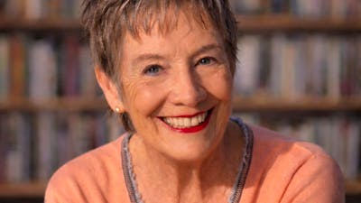 A smiling, mature woman with short, gray hair, looking directly at the camera in front of a blurred