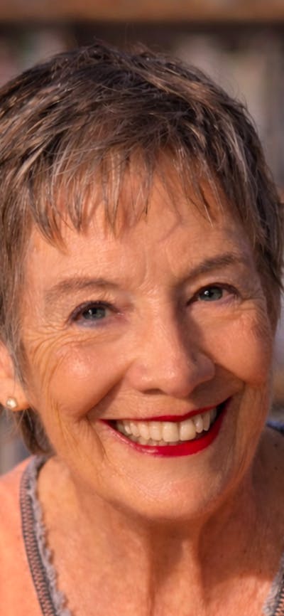 A smiling, mature woman with short, gray hair, looking directly at the camera in front of a blurred
