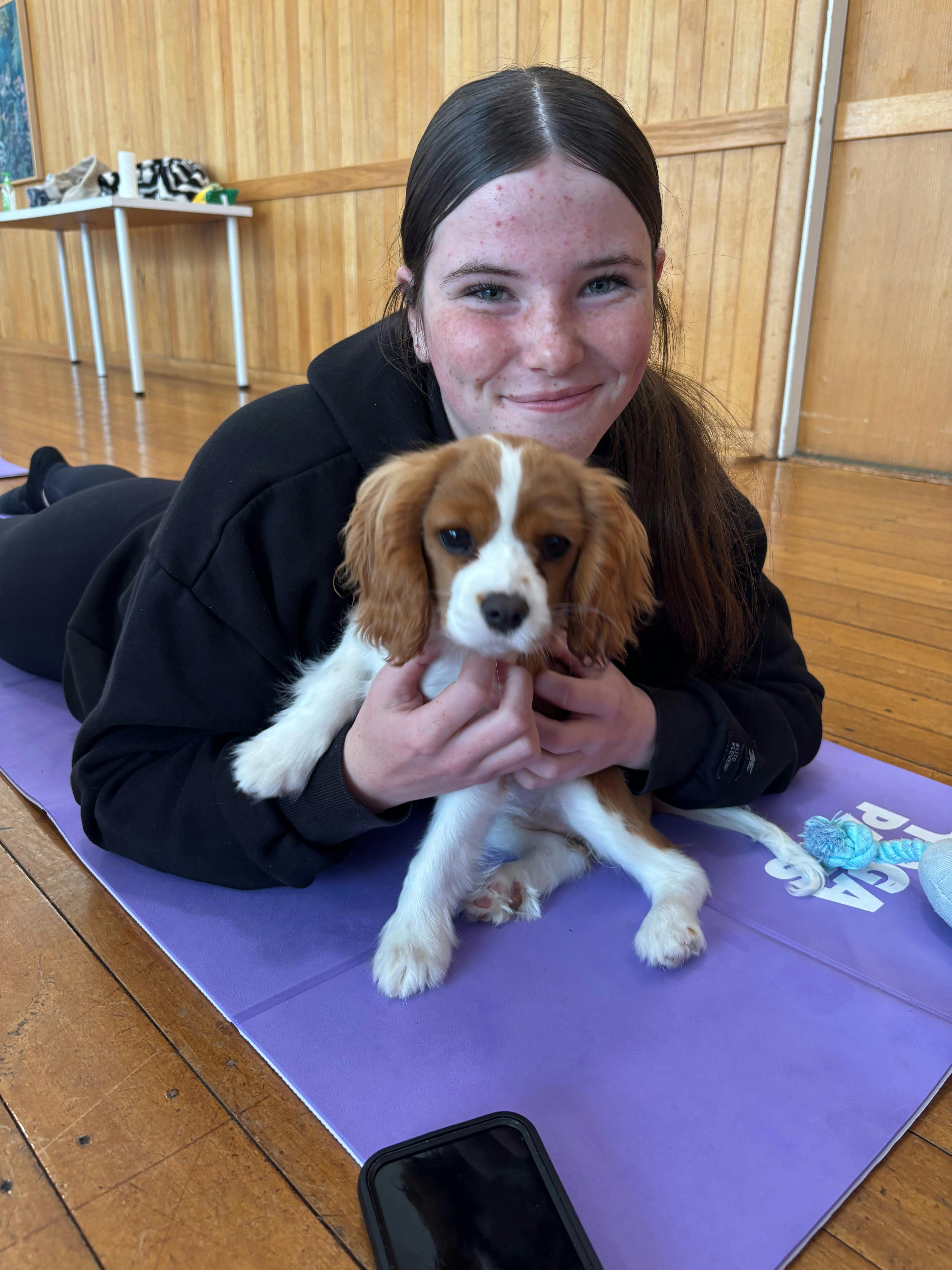 A smiling participant sits on a purple mat holding a brown and white puppy.