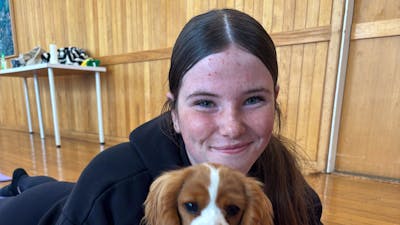 A smiling participant sits on a purple mat holding a brown and white puppy.