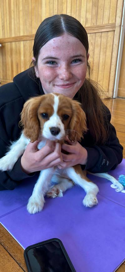 A smiling participant sits on a purple mat holding a brown and white puppy.