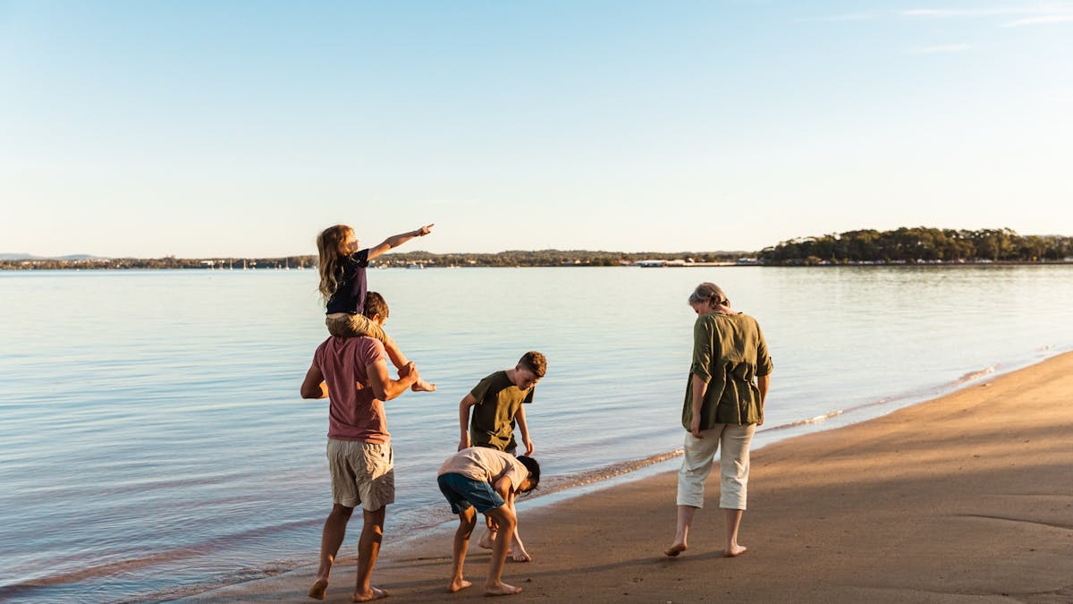 Family walking along Coochiemudlo Island beach, kids exploring shells and sand