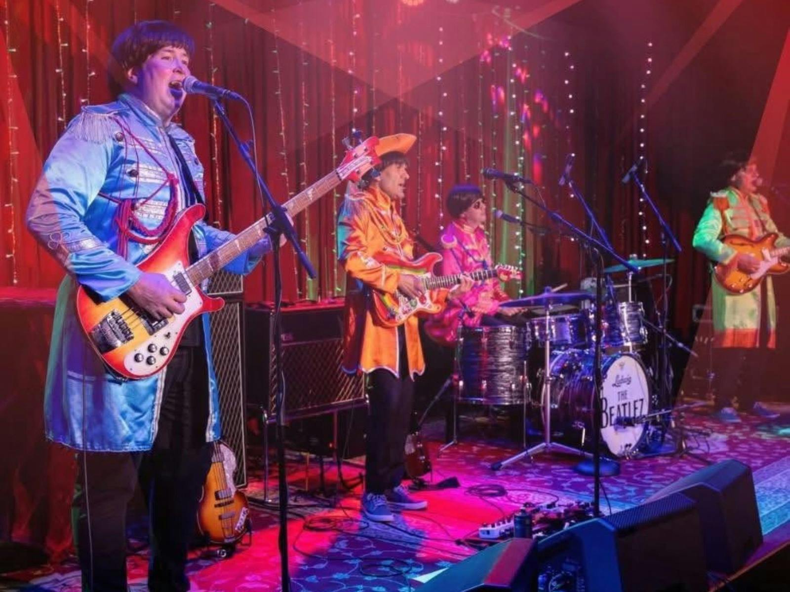 4 band members playing musical  instruments and singing on stage