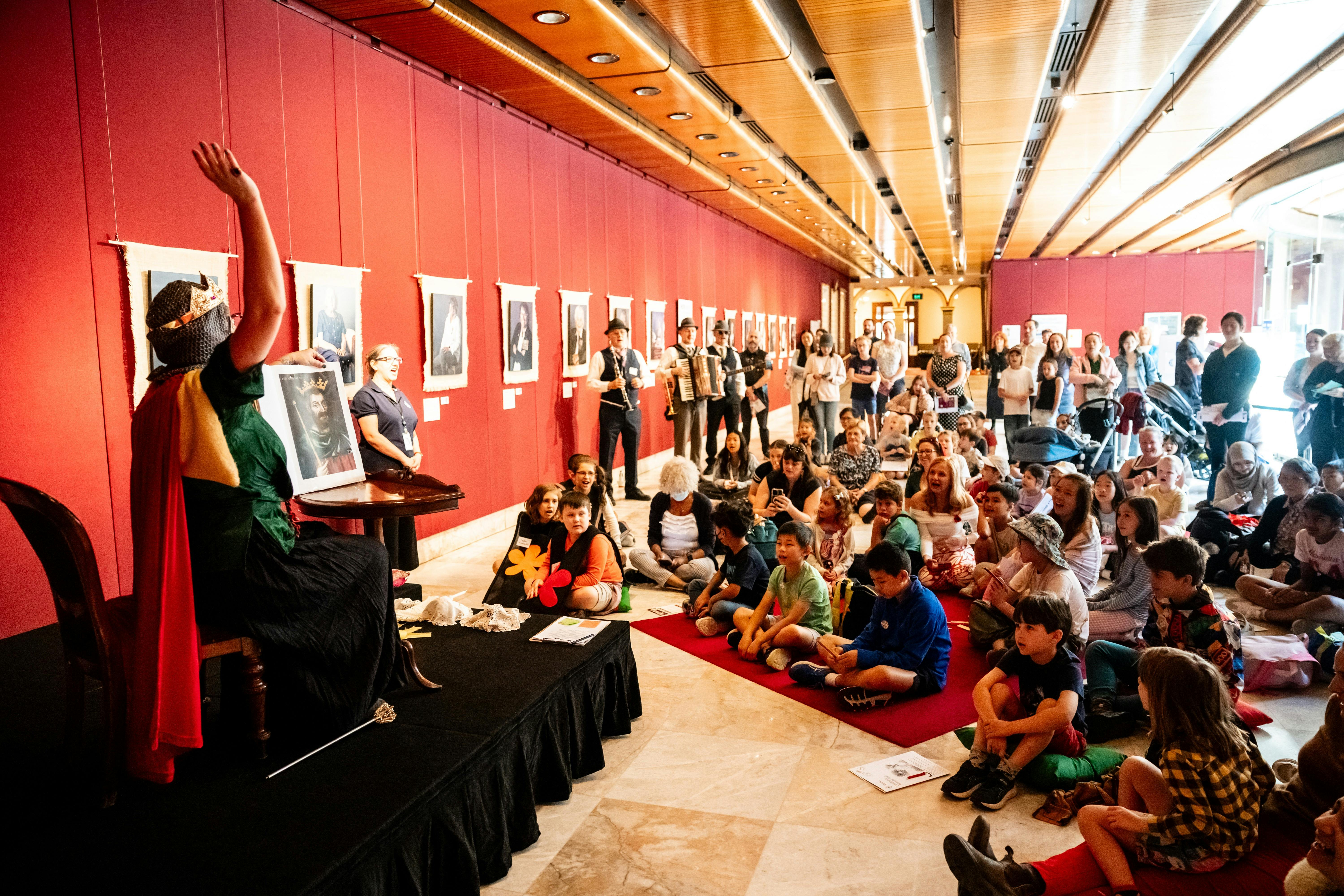 Children sit cross legged on the floor and watch a performer at Family Fun Day NSW