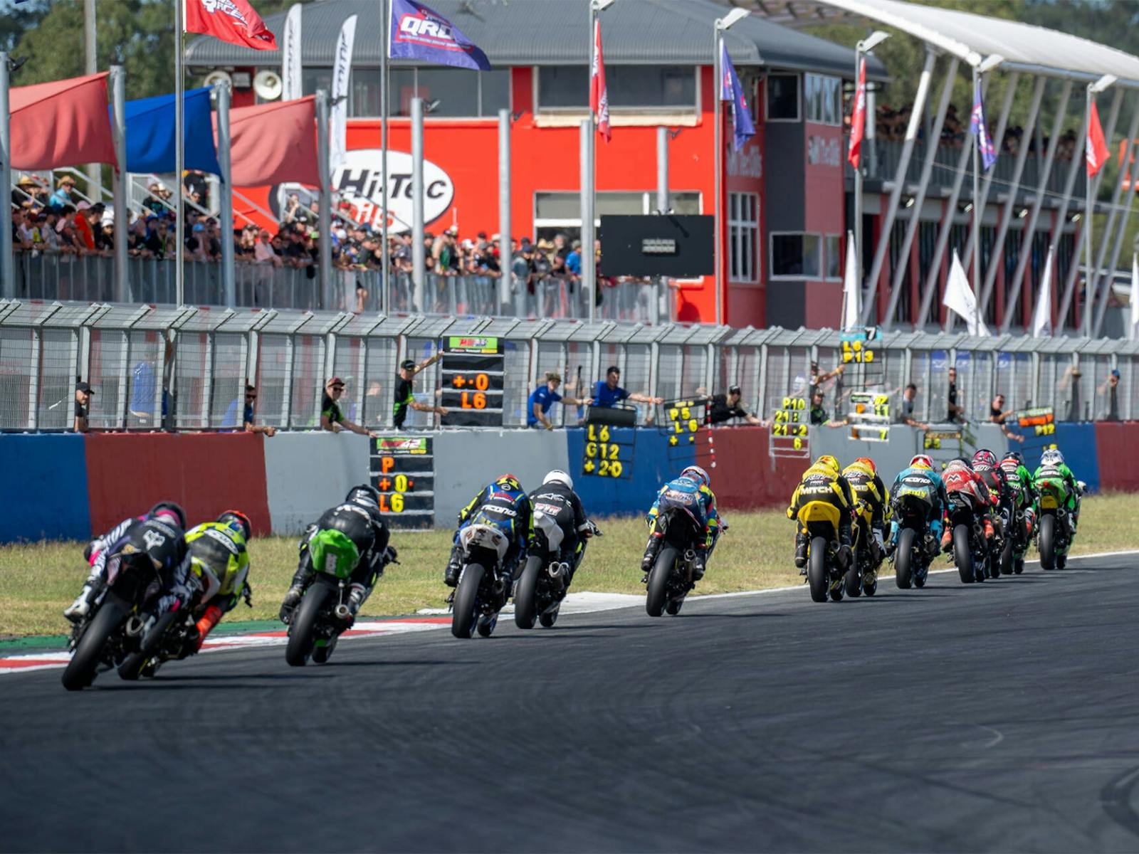 Bikes race down the main straight as a crowd cheers Bikes race down the main straight as a crowd cheers