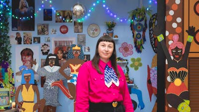 A person wearing a pink shirt stands in front of an 3D artwork featuring a disco ball and figures.