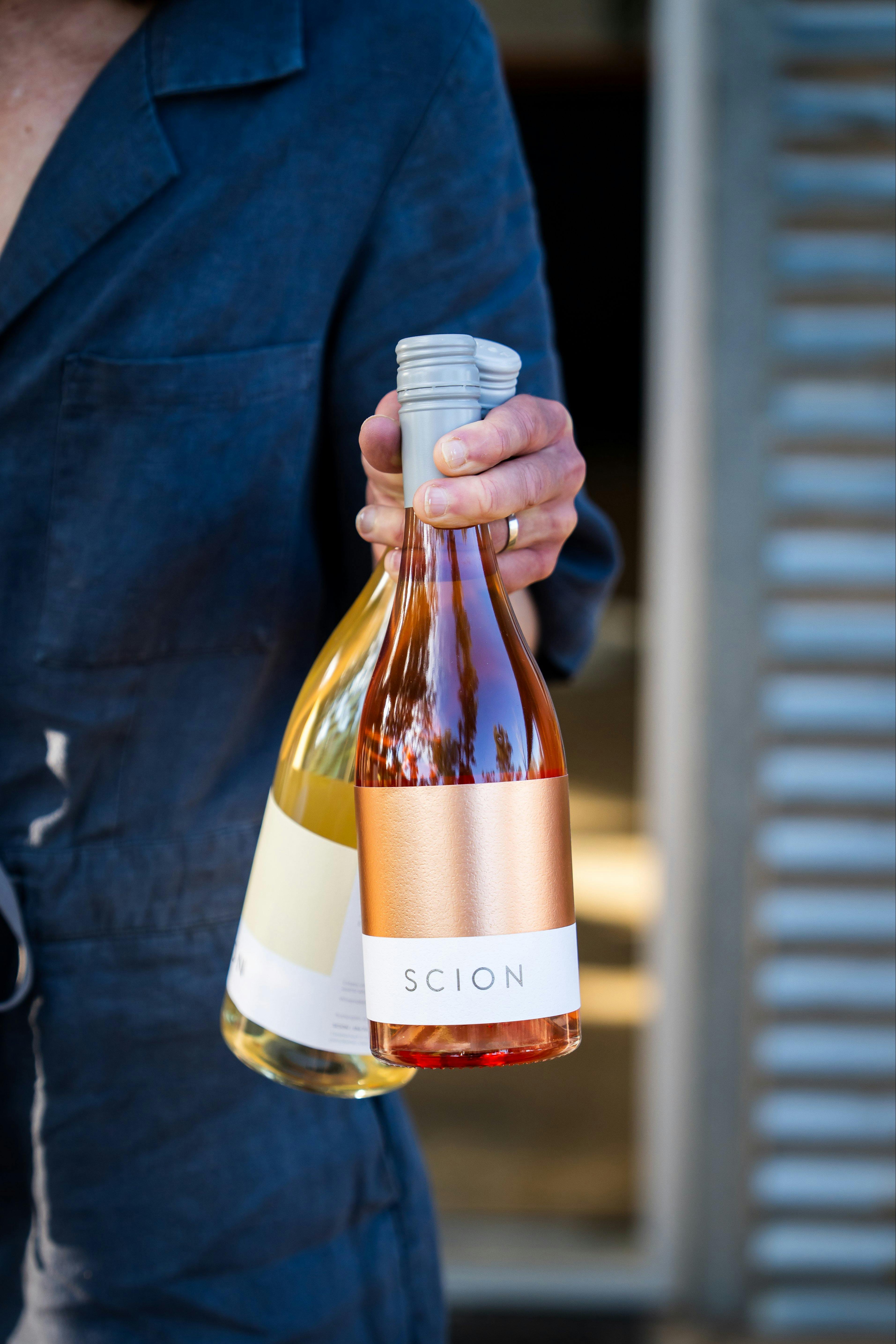 Crop of hand holding two wine bottles with coloured Scion labels