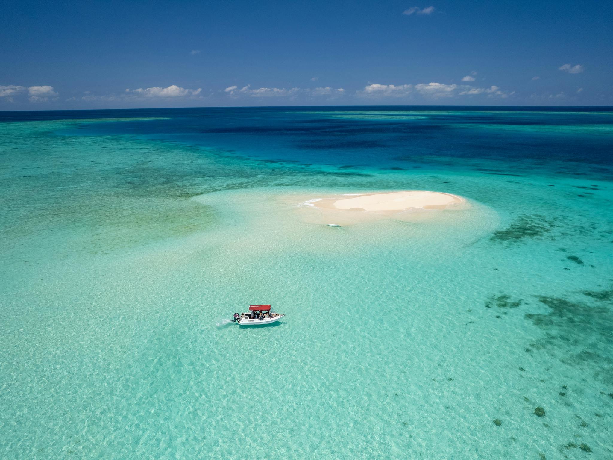 A boat approaches a sand cay surrounded by tropical blue seas.