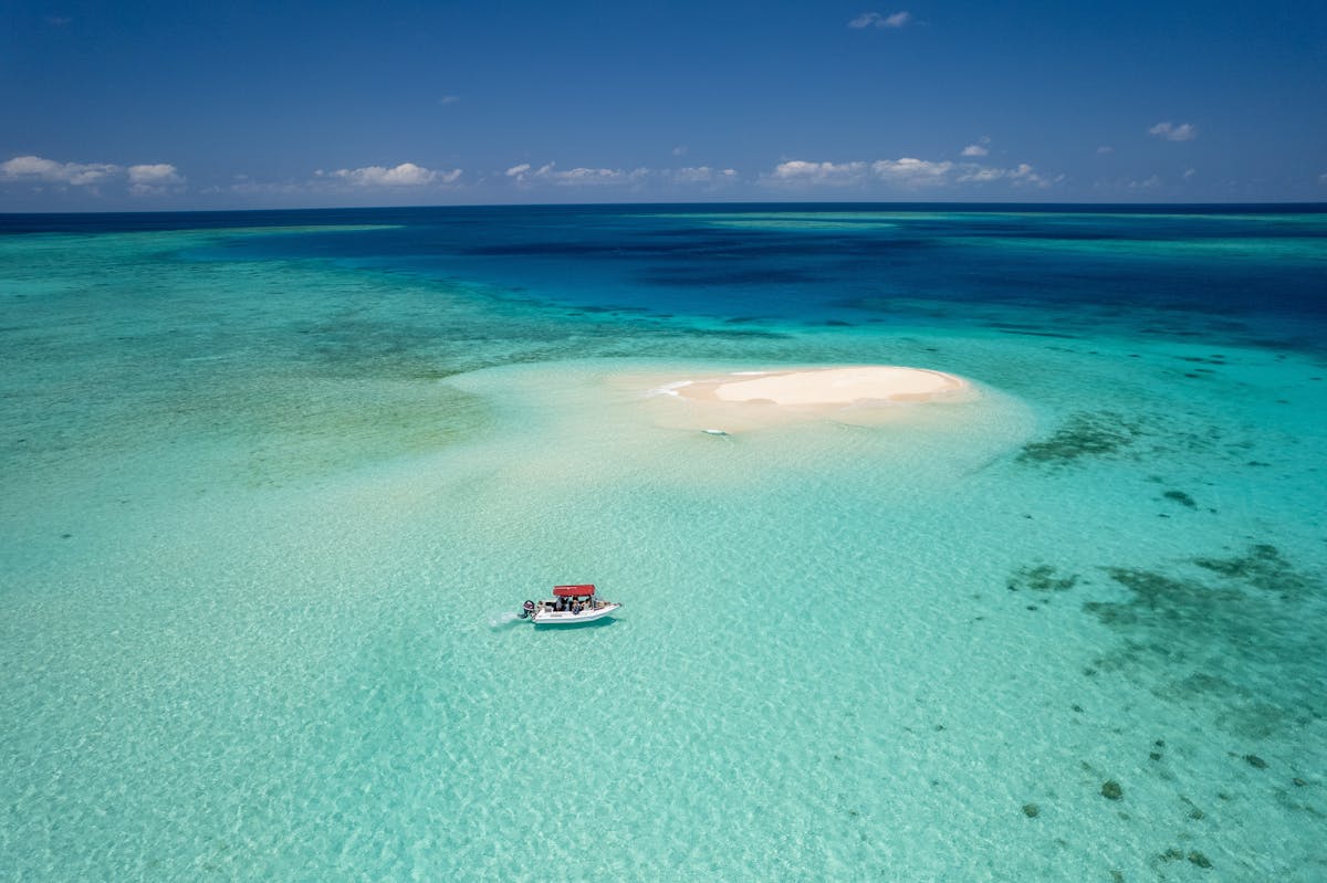 A boat approaches a sand cay surrounded by tropical blue seas.