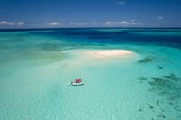A boat approaches a sand cay surrounded by tropical blue seas.