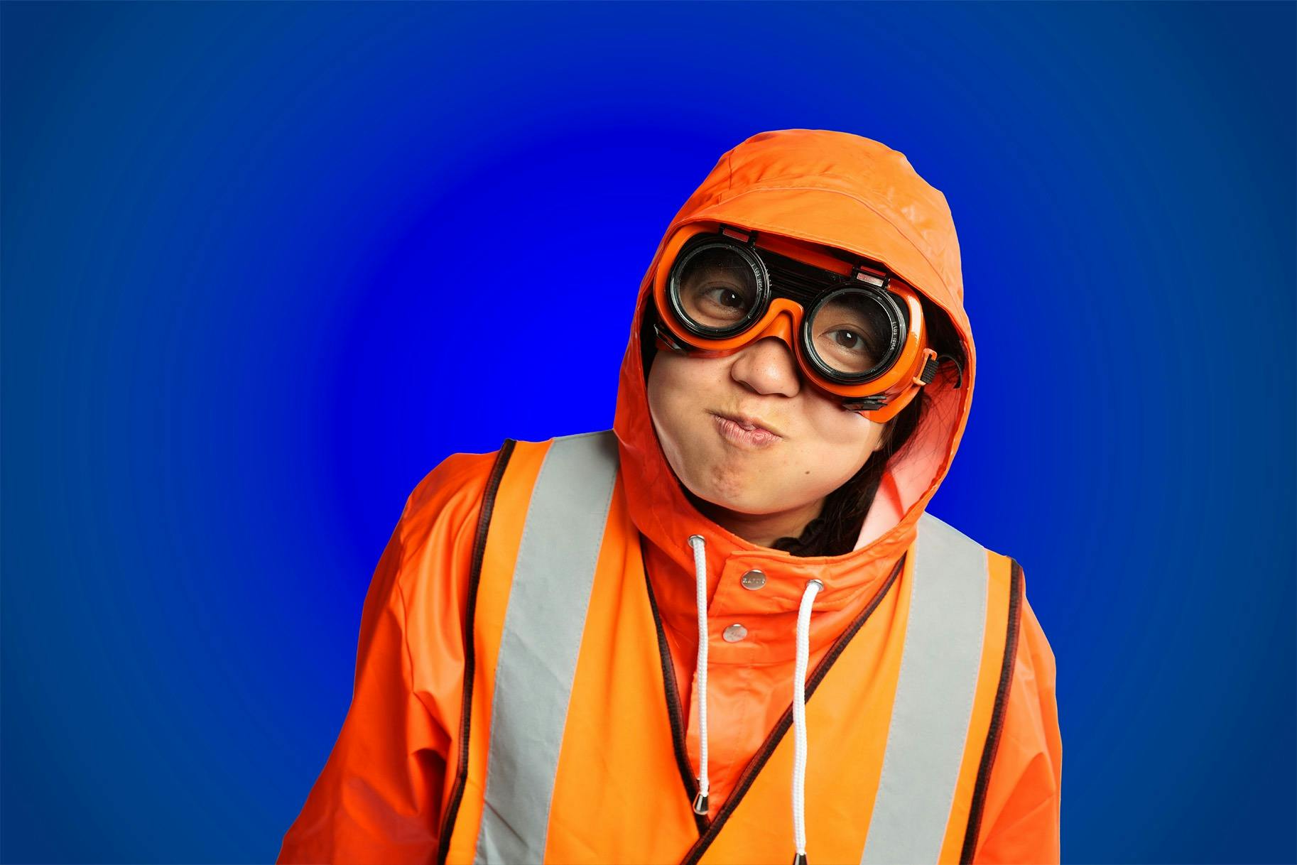 A person dressed in bright orange wet weather gear and goggles is holding their breath on a blue