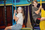 A boy and girl smiles as they enjoy swinging in the fixed play structure