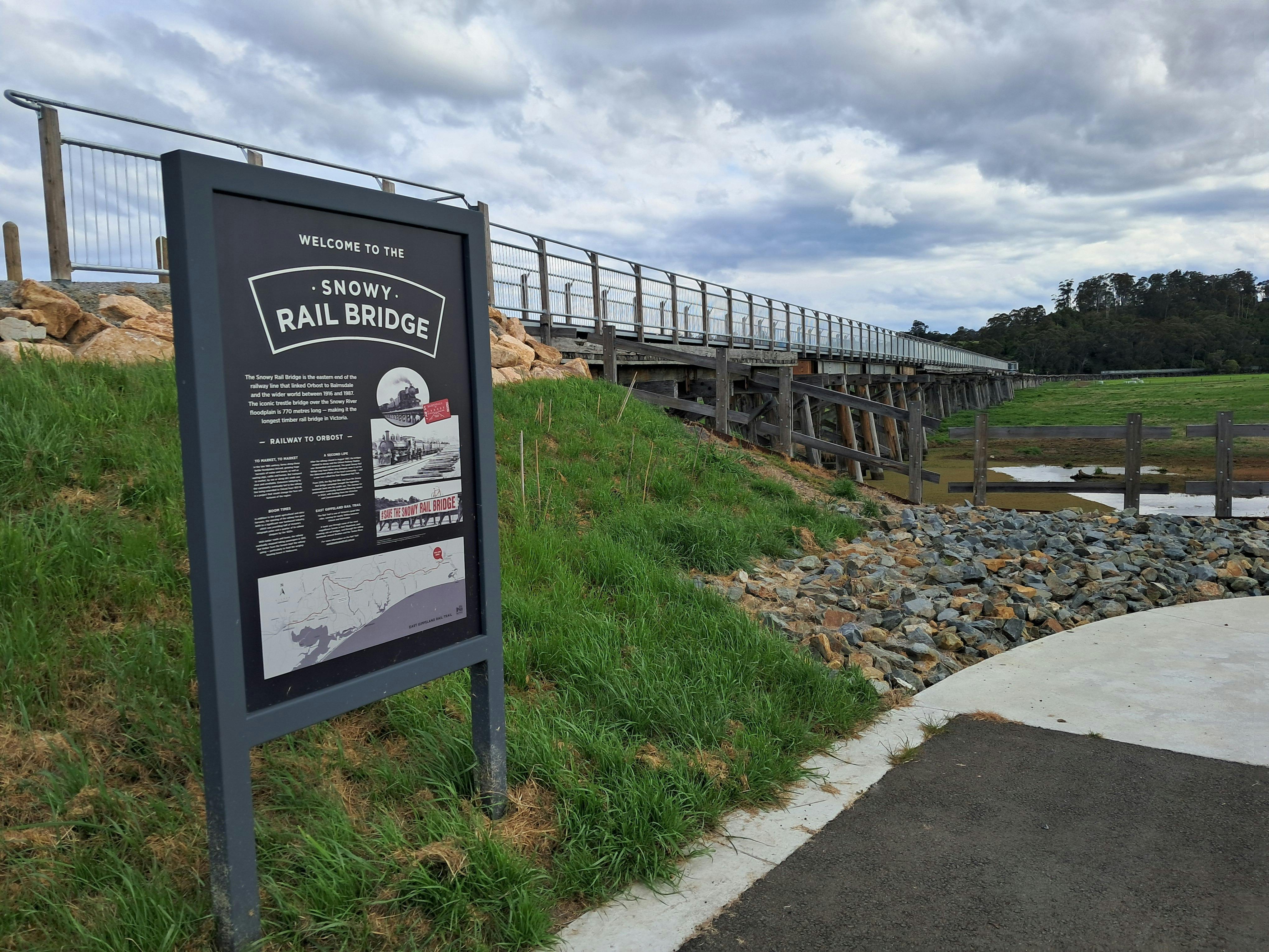 An information sign on embankment leading to modern pathway on top of timber rail bridge